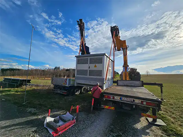 Kranarbeiten auf einer Baustelle im Freien, mit Bauarbeiter, bei sonnigem Himmel.